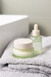 Light green dropper bottle and cream jar on light grey bath towel near basin closeup