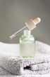 Drop falls from a pipette resting on a bottle filled with green serum on grey towel in bath