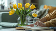 Female hands with vase of yellow tulips glass and book