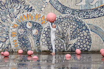 Wall Mural - Young hairless girl with alopecia in white futuristic suit dancing outdoor smoothly holding pink ball on abstract mosaic Soviet background, symbolizes self expression and cultural identity