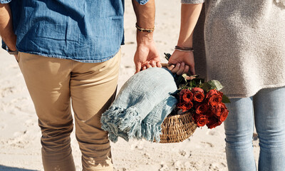 Wall Mural - Couple, beach and picnic basket with flowers in walking, back and holiday for vacation, ocean and cropped shot. Romantic, summer and red roses, bonding and sea or outdoor, sand and romance in love