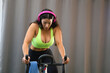 Young and beautiful brunette woman training on the bike in the gym. The girl is listening to music on her headphones. She is dressed in a top and bikini bottoms. Concept of health and sport.