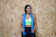 Young and beautiful brunette woman resting leaning against the gym wall. She has a towel around her neck and is dressed in a top and leggings. Concept of health and sport.