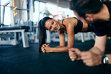 Fototapeta Pomosty - Gym couple doing abs together, holding a plank, looking at each other, smiling.