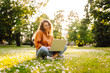 © maxbelchenko - Portrait of attractive young woman sitting on green grass in park while using laptop and wireless earphone. Freelancer, education, online, technology concept.
