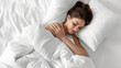 Woman sleeping comfortably in bed, wrapped in white sheets and pillows