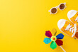 A vibrant summer themed photo featuring a colorful pinwheel, orange sneakers, and white sunglasses laid out on a yellow background