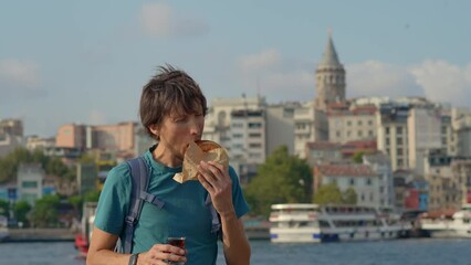 Wall Mural - A young traveler relishes a bite of a crusty simit and sips Turkish tea at a pier with seagulls fluttering by and the iconic Galata Tower looming in the backdrop.