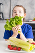 Cute little girl eating lettuce in the kitchen of the house, in front of her is a plate of fresh vegetables. Selected focus.