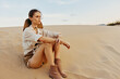 Woman standing confidently on sandy dune with hands on hips amidst vast desert landscape