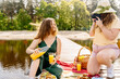 Two happy women in shorts and yellow hat having a picnic on a dock by the water