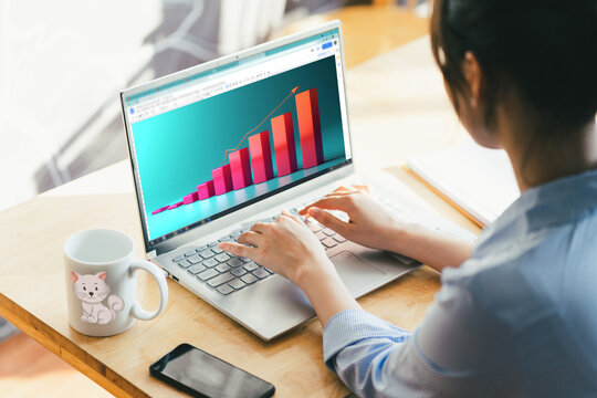 Jóven mujer trabajando en su laptop, graficando sus ventas y ganancias en un gráfico de barras con tendencia creciente. Escritorio con taza de café y teléfono móvil a su lado.