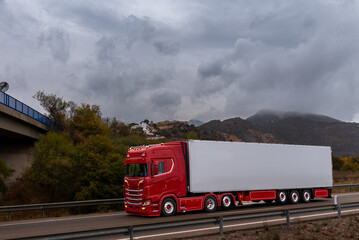 Wall Mural - Eye-catching truck with a refrigerated semi-trailer and two drive axles traveling on a highway, with a sky threatening a storm.