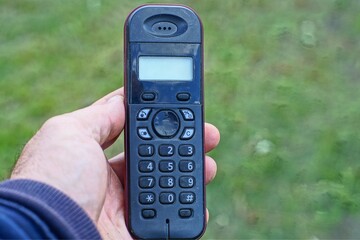 Wall Mural - one old push-button with a display, plastic, simple black radiotelephone with an antenna in the hand on the street  outside during the day