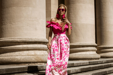 Wall Mural - Elegant, stylish woman in pink floral dress and sexy high heels is sensually walking in the city on a sunny summer day. Outdoor shoot.