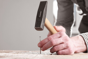 Wall Mural - Professional repairman hammering nail into wooden board indoors, closeup