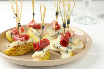 Wall Mural - Tasty canapes with pears, blue cheese and prosciutto on white wooden table, closeup