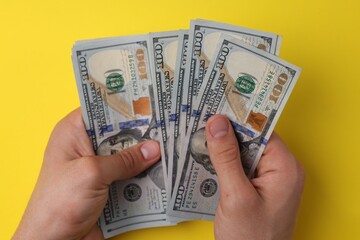 Wall Mural - Money exchange. Man holding dollar banknotes on yellow background, top view