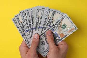 Wall Mural - Money exchange. Man holding dollar banknotes on yellow background, top view