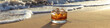 Whiskey or bourbon glass on a sandy beach with sea waves in the background. Alcoholic drink on tropical island.