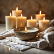 A collection of lit candles, with some placed on a table and others on a towel. A bowl is also present among the candles.