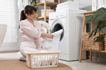 Canvas Print - Happy young housewife putting laundry into washing machine at home