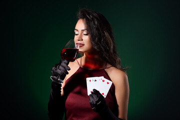 Wall Mural - Beautiful young African-American woman with playing cards and glass of wine on dark green background