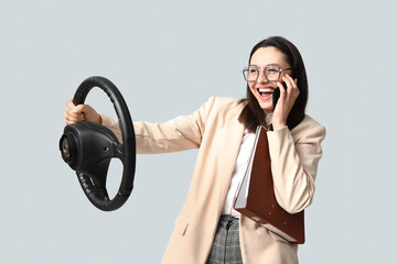 Canvas Print - Happy businesswoman with steering wheel and documents talking by phone  on light background