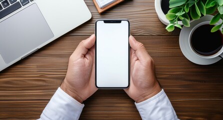Wall Mural - Close up of man's hands holding blank white smartphone with empty screen over office desk, laptop on background, closeup shot, high angle view.