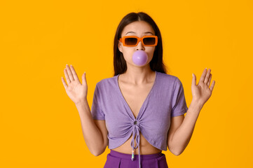 Poster - Beautiful surprised Asian woman with chewing gum on yellow background