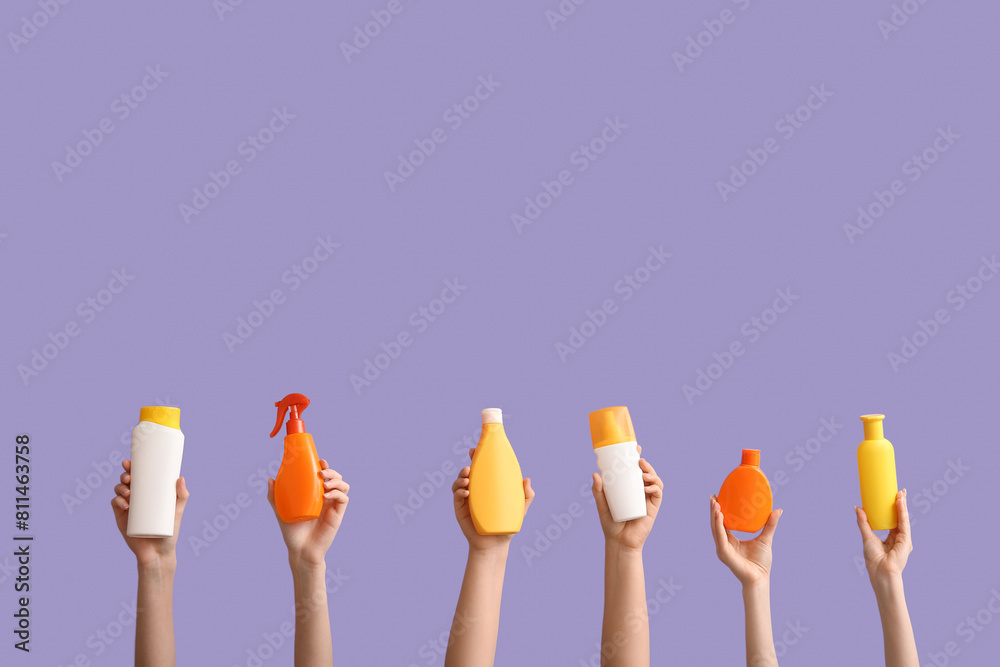 Female hands with different sunscreens on violet background. Travel concept.