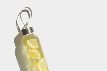 Wall Mural - Lemon water drink detox in glass bottle at sunlight on white background. Wellness, diet, eating healthy concept. Stylish reusable water bottle, eco friendly lifestyle minimal trend photo