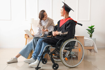 Wall Mural - Male graduate in wheelchair with his friend using laptop at home