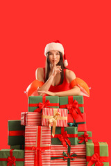 Poster - Young woman in Santa hat with swim armbands and gifts showing silence gesture on red background. Christmas in July