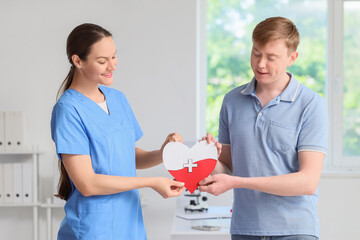 Wall Mural - Male blood donor with nurse holding paper heart in clinic