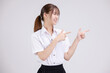 Pretty Asian woman in university student uniform over isolated white background pointing finger to the side.