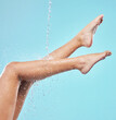 Legs, water and woman in studio with natural, wellness or health routine for self care in morning. Beauty, hygiene and female person with liquid splash on body for washing skin by blue background.