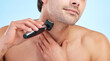 Hands, shaving and man with electric razor on studio backdrop for personal hygiene and skin care. Male person, beauty and grooming by blue background for beard, hair removal and epilation or cosmetic