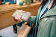 Close up of unrecognizable woman client holding wallet with bow and ecological shopping paper bags in front of a counter on local store. Female customer ready to pay purchased items on small business.