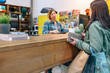 Female client taking credit card to pay purchased items while talking with woman shop assistant on store. Small business and local commerce concept. Selective focus on customer. Left copy space.