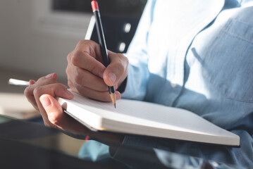 Wall Mural - Woman hand with a pencil writing on paper notebook. Female student taking note on lecture chair during studying in classroom. business planning, to do list reminder