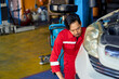 Asian technician man in red suit try to repair a white car in car garage service.