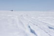 Winter road in the tundra. View of a winter road in the snowy tundra in the Arctic. An abandoned house in the distance. Desert winter arctic landscape. White silence. Tread marks in the snow.
