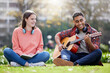 Outdoor, students and man with guitar, university and happiness with sunshine, friends and cheerful. Study break, woman and guy with instrument, musician and relax with joy, summer and grass field