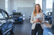 Portrait of a female car saleswoman working in the showroom. Close up of a businesswoman offering a handshake in the showroom. Female manager in car dealership