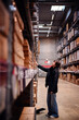 © Oleksii Yemelianov - Young woman reaching towards a high shelf in a warehouse, illustrating her focus and determination. Her casual attire