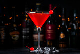 Fototapeta Na sufit - Red alcoholic cocktail drink with cherry on dark background, bar counter with bottles