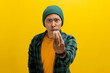 © Jamaludinyusup - Annoyed young Asian man, dressed in a beanie hat and casual shirt, makes the Italian hand gesture, pinching his fingers together, while standing against a yellow background