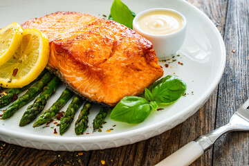 Sticker - Fried salmon steak with cooked green asparagus and mayonnaise served on wooden table
