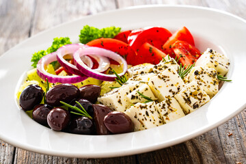 Wall Mural - Greek style salad - fresh vegetables with feta cheese and kalamata olives served in white bowl on wooden table
